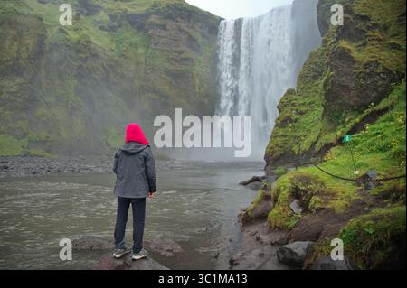 Eine ältere Frau, die vor dem Wasserfall in Island steht Stockfoto
