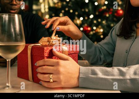 Eine detaillierte Nahaufnahme der Hände einer Frau, die eine rote Weihnachtsgeschenkbox auspackt, um den Moment der Vorfreude und Überraschung während einer festlichen Ho festzuhalten Stockfoto