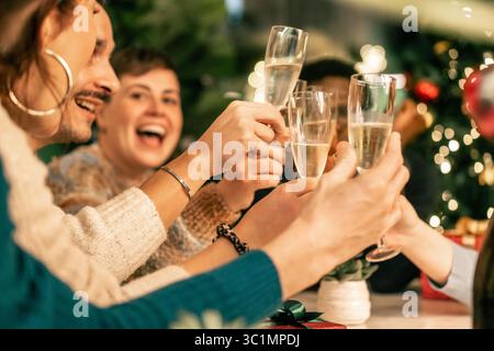 Eine fröhliche, vielfältige Gruppe junger Freunde lacht, während sie bei einer festlichen Weihnachtsfeier zu Hause ein Glas Champagner anstoßen. Stockfoto