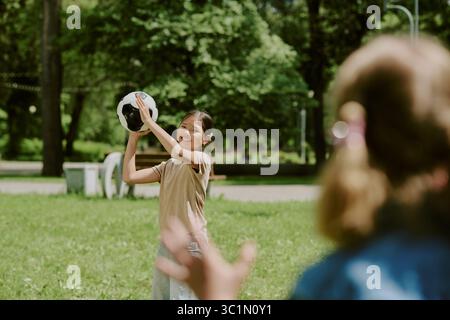 Lächelndes asiatisches Mädchen wirft Fußball zu Freund im Park Stockfoto