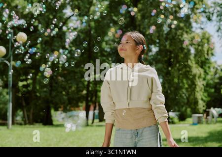 Porträt eines lächelnden asiatischen Mädchens, während er draußen zwischen Seifenblasen steht Stockfoto