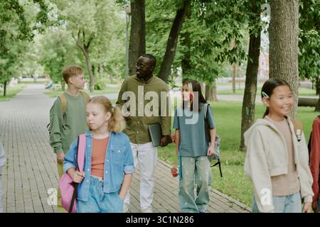 Verschiedene Gruppe von Kindern und Schwarzen männlichen Lehrern, die gemeinsam im Park spazieren gehen Stockfoto