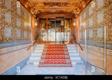 Luxuriöser Eingang zum Barcelona-Gebäude mit rotem Teppichboden. Verzierte Wände, Detaillierte Holzarbeiten. Historische Spanische Architektur, Elegantes Urban Inter Stockfoto