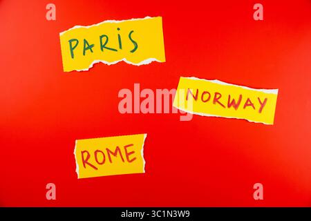 Farbenfrohe Papierausschnitte von Stadtnamen Paris, Rom und Norwegen sind künstlerisch auf einem leuchtend roten Hintergrund angeordnet, um Reisemotive und Projekte zu kreieren Stockfoto
