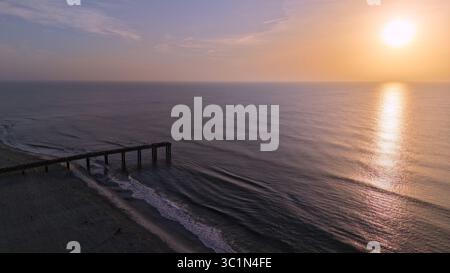 Blick aus der Vogelperspektive auf den ruhigen Pier von Saint Johns County, der sich in das ruhige Meer unter dem warmen Glanz der aufgehenden Sonne erstreckt, Saint Augustine Beach, Florida, USA. Stockfoto