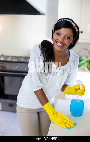 Afroamerikanerin, die Handschuhe trägt, die Küchenzeile mit einem Tuch abwischt, während sie die Sprühflasche hält Stockfoto