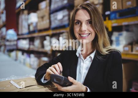 Weibliche Frau im Blazer-Scanning-Karton mit Barcode-Scanner im Ablagegang, Kopierraum Stockfoto