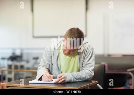 Notizbuch und Bleistift liegen auf einem hölzernen Schreibtisch im Klassenzimmer in der Nähe von Whiteboard und Kopierraum Stockfoto