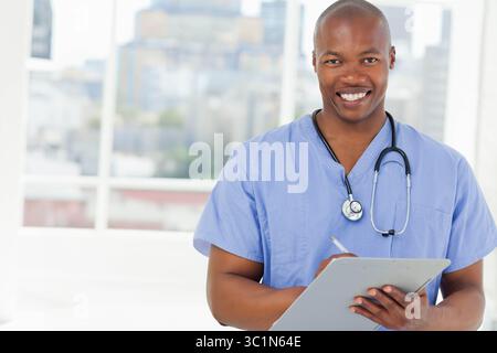 Afroamerikaner Arzt schreibt Notizen auf Klemmbrett mit Stethoskop im Klinikraum, Kopierraum Stockfoto