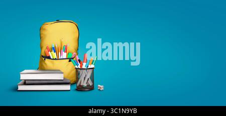 Eine Back-to-School-Szene aus einem Stapel von drei Lernbüchern, gelber Schultasche, Stiften und Bleistiften vor blauem Hintergrund mit Kopierraum. Stockfoto