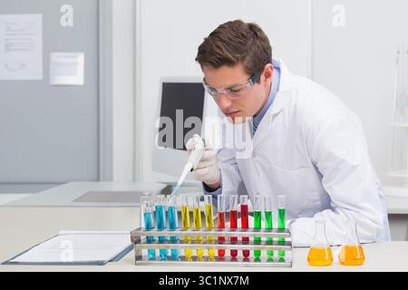 Erwachsener Wissenschaftler, der Flüssigkeit mit einer Pipette in das Reagenzglasgestell auf dem Labortisch mit Kolben abgibt Stockfoto