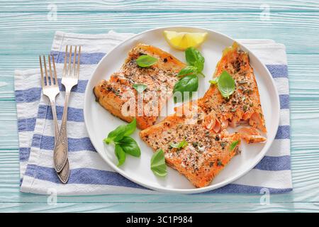 Gegrillte ganze Lachsfilets mit Haut auf einem Teller mit frischem Basilikum, Zitronenscheiben, Gabeln auf Holztisch, horizontale Ansicht von oben, keine KI generiert Stockfoto