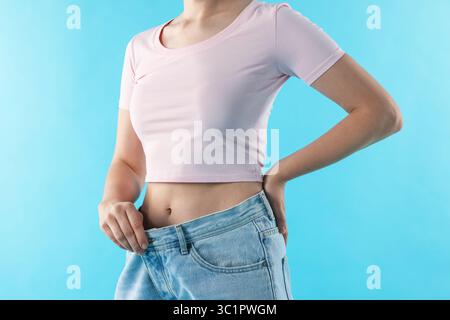 Frau trägt alte Jeans nach Gewichtsverlust auf hellblauem Hintergrund, Nahaufnahme Stockfoto
