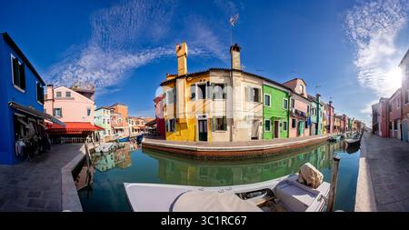 Bunte Häuser spiegeln sich an einem klaren, sonnigen Tag im ruhigen Kanal von Burano, Venedig, wider Stockfoto