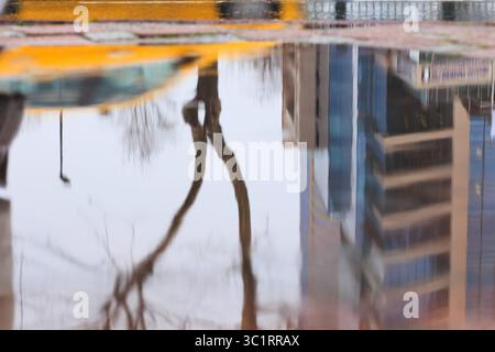 Reflexion eines Gebäudes und eines gelben Taxis in einer Pfütze, abstrakter Hintergrund. Stockfoto