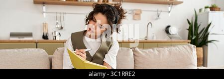 Die Frau mit lockigen Haaren konzentrierte sich auf ihr Notebook, tauchte in eine stilvolle Wohnumgebung ein, Banner Stockfoto