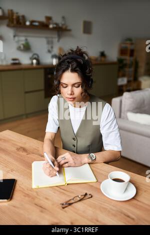Eine junge Frau mit lockigen Haaren konzentriert sich auf ihr Notizbuch, eingetaucht in das Studium zu Hause. Stockfoto