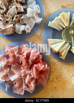 Stücke von herzhaftem, typisch italienischem Schinken, Salami und Käse auf blauen Tellern auf dem Tisch. Traditionelle italienische Küche. Direkt darüber. Stockfoto