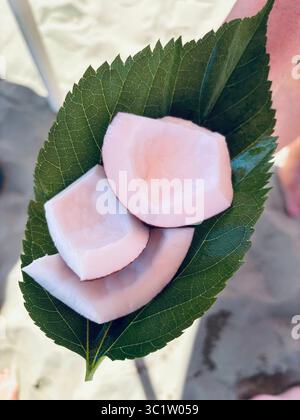 Hand hält an einem Blatt Kokosnussstücke am Strand. Ein typischer Snack am Strand. Sommeressen. Stockfoto