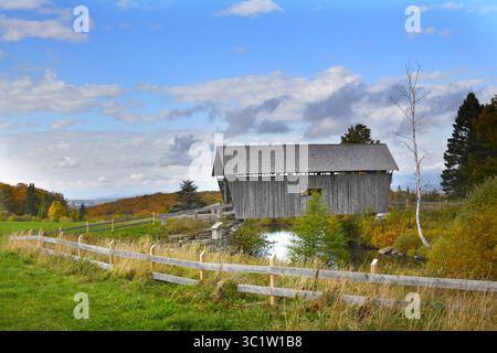 A. M. Foster Covered Bridge befindet sich in Cabot, Vermont. Er erstreckt sich über einen kleinen Teich und ist verwittert und verblasst aus Holz gebaut. Der Herbst bedeckt die Berge Stockfoto