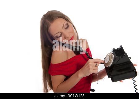 Eine junge Frau führt einen Anruf, während sie elegant ein Retro-Telefon benutzt, in Rot gekleidet. Stockfoto