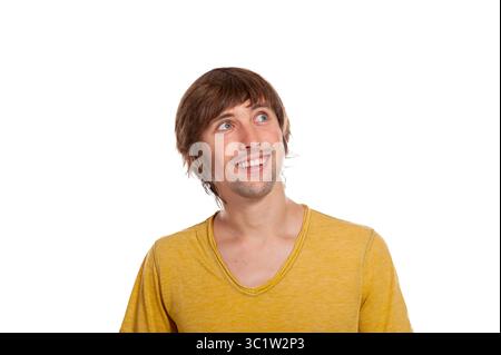 Ein fröhlicher junger Mann mit hellgelbem Hemd bringt Staunen zum Ausdruck, während er nach oben blickt. Stockfoto
