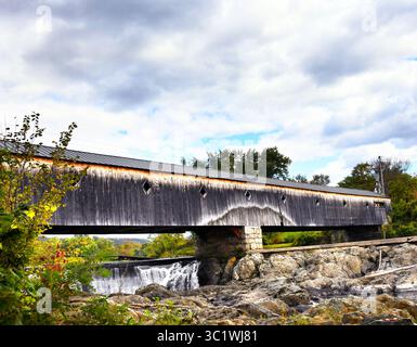 Die Haverhill-Bath Covered Bridge in Bath, New Hampshire, ist lang, verwittert und verblasst. Überlauf ist unter der Brücke zu sehen. Stockfoto