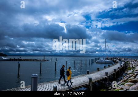 23. Juli 2025, Mecklenburg-Vorpommern, Timmendorf (insel Poel): Im Segelhafen auf der Insel Poel sind Wanderer vor dem Hintergrund dunkler Wolken unterwegs. In Norddeutschland gibt es starke Regenschauer, Temperaturen von rund 20 Grad und starke Winde. Foto: Jens Büttner/dpa Stockfoto