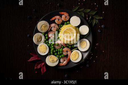 Ein dunkles, stimmungsvolles Foto zeigt einen schwarzen Teller mit einem lebhaften Arrangement aus Meeresfrüchten und Gemüse. Ein perfekt gekochtes hartgekochtes Ei sitzt Stockfoto