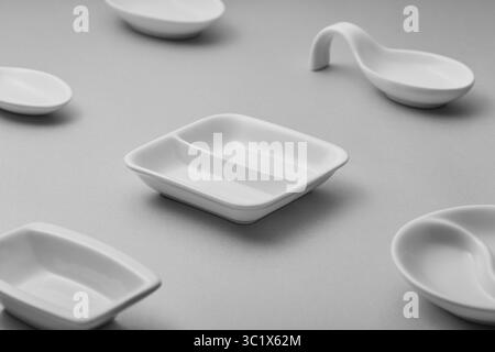 Ein minimalistisches Stillleben mit einer Kollektion weißer Keramikschalen auf einer hellgrauen Oberfläche. Die Gerichte variieren in Form und Größe, Stockfoto
