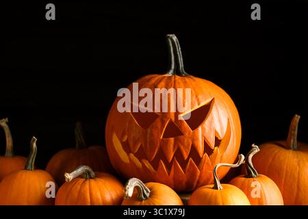 Halloween-Komposition mit geschnitztem Gesichtskürbis und orangefarbenen Minis auf dunkler Oberfläche. Gruselige saisonale Einrichtung für Herbstferien und stimmungsvolle Feierlichkeiten Stockfoto