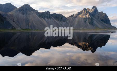 Der majestätische Vestrahorn Mountain erhebt sich dramatisch in der Nähe von Stokksnes, mit seiner atemberaubenden Reflexion im ruhigen Wasser. Während der goldenen Stunde zeigt die Szene die natürliche Schönheit Islands. Stockfoto