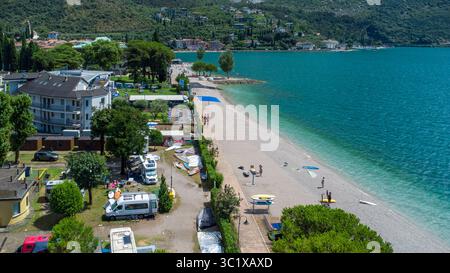 Nago-Torbole, Trentino, Italien - 21. Juli 2025: Aus der Vogelperspektive auf den Campingplatz und den Strand in Nago-Torbole am Gardasee. Camper, Windsurfer und Badende genießen das klare Wasser und die entspannte Atmosphäre direkt am Seeufer *** Luftaufnahme vom Campingplatz und Strand in Nago-Torbole am Gardasee. Wohnmobil, Windsurfer und Badegäste genießen das klare Wasser und die entspannte Atmosphäre direkt am Seeufer Stockfoto