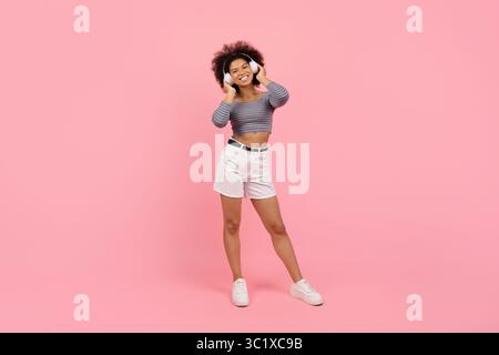 Aufnahme einer glücklichen afroamerikanischen Frau in voller Länge in Kopfhörern, die Musik genießt Stockfoto