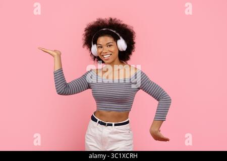 Fröhliche junge Frau mit schnurlosen Kopfhörern, Gesten und Tanzen Stockfoto