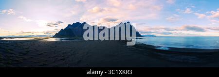 Wellen schlagen sanft gegen den schwarzen Sandstrand von Stokksnes, während der Berg Vestrahorn im Hintergrund dramatisch aufsteigt. Die Dämmerung strahlt einen magischen Glanz aus, der die friedliche Landschaft Islands bereichert Stockfoto