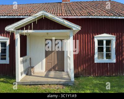 Bezauberndes rotes Haus mit einer weißen Veranda und einer rustikalen Atmosphäre an einem sonnigen Tag. Stockfoto