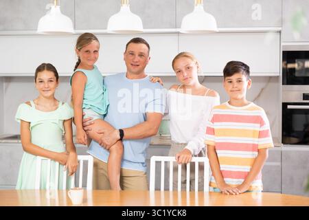 Glücklicher Vater mit drei Töchtern und Sohn steht neben dem Küchentisch. Stockfoto