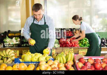 Mann Verkäufer, der im Supermarkt arbeitet und Äpfel auf der Theke verteilt Stockfoto