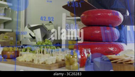 Männlicher Verkäufer auf Schürze, der Käse in einer Käserei mit Rotwachsrädern, Olivengläsern, Kopierraum inspiziert Stockfoto