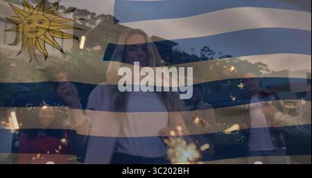 Mit Glitzern, Gruppe von sechs Erwachsenen, die in der Abenddämmerung im Garten feiern, mit uruguayischer Flagge Stockfoto