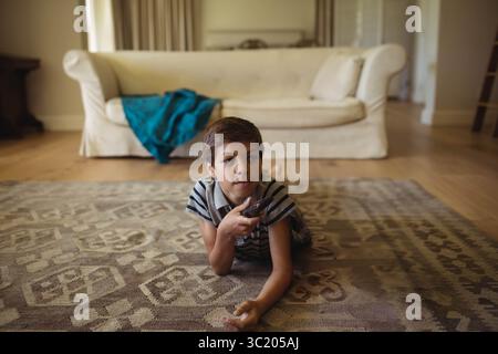 Junge, der auf gemustertem Teppich im Wohnzimmer liegend, mit Fernbedienung und Fernsehen Stockfoto