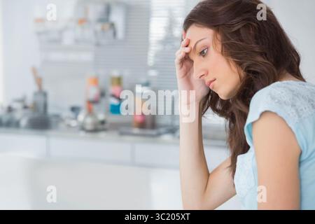 Frau, die sich Kopf auf die Hand an der Küchentheke lehnt, mit Gewürzgläsern und Edelstahl-Backsplash Stockfoto