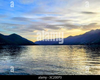 Warmer Sonnenuntergang am Lago Maggiore Ascona mit gelben Sonnenstrahlen im Wasser und Hügeln im Hintergrund Stockfoto