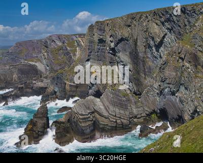 Dramatische Klippen erheben sich vor einem klaren blauen Himmel in Mizen Head, Irland, mit Wellen, die unter ihnen abstürzen. Fängt die raue Schönheit der Küste ein. Stockfoto