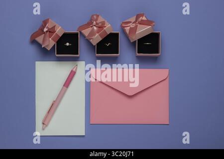 Goldene Ringe in einer Geschenkbox, Umschlag mit Hochzeitseinladungen auf lila Hintergrund. Draufsicht. Flache Lagen Stockfoto