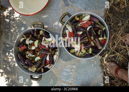 Blick von oben auf das ungekochte „Melitzanes giaxni“, ein traditionelles griechisches Rezept mit Auberginen, Tomaten, Zwiebeln und Olivenöl, das in zwei Metallblechen angeordnet ist. Stockfoto