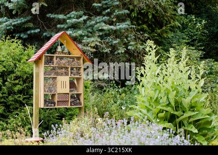 Holzinsektenhotel in einem Garten, gefüllt mit Tannenzapfen, Stroh und Zweigen - ein Zufluchtsort für Bestäuber und Insekten. Stockfoto