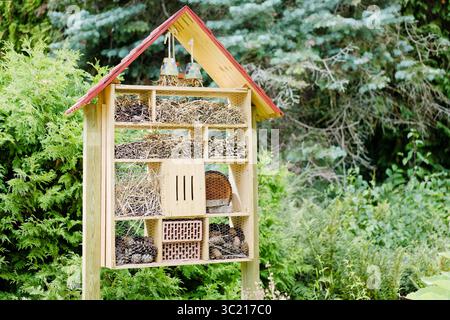 Holzinsektenhotel in einem Garten, gefüllt mit Tannenzapfen, Stroh und Zweigen - ein Zufluchtsort für Bestäuber und Nützlinge. Stockfoto