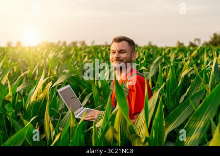Bauer, der auf grünem Maisfeld steht und am Laptop arbeitet Stockfoto